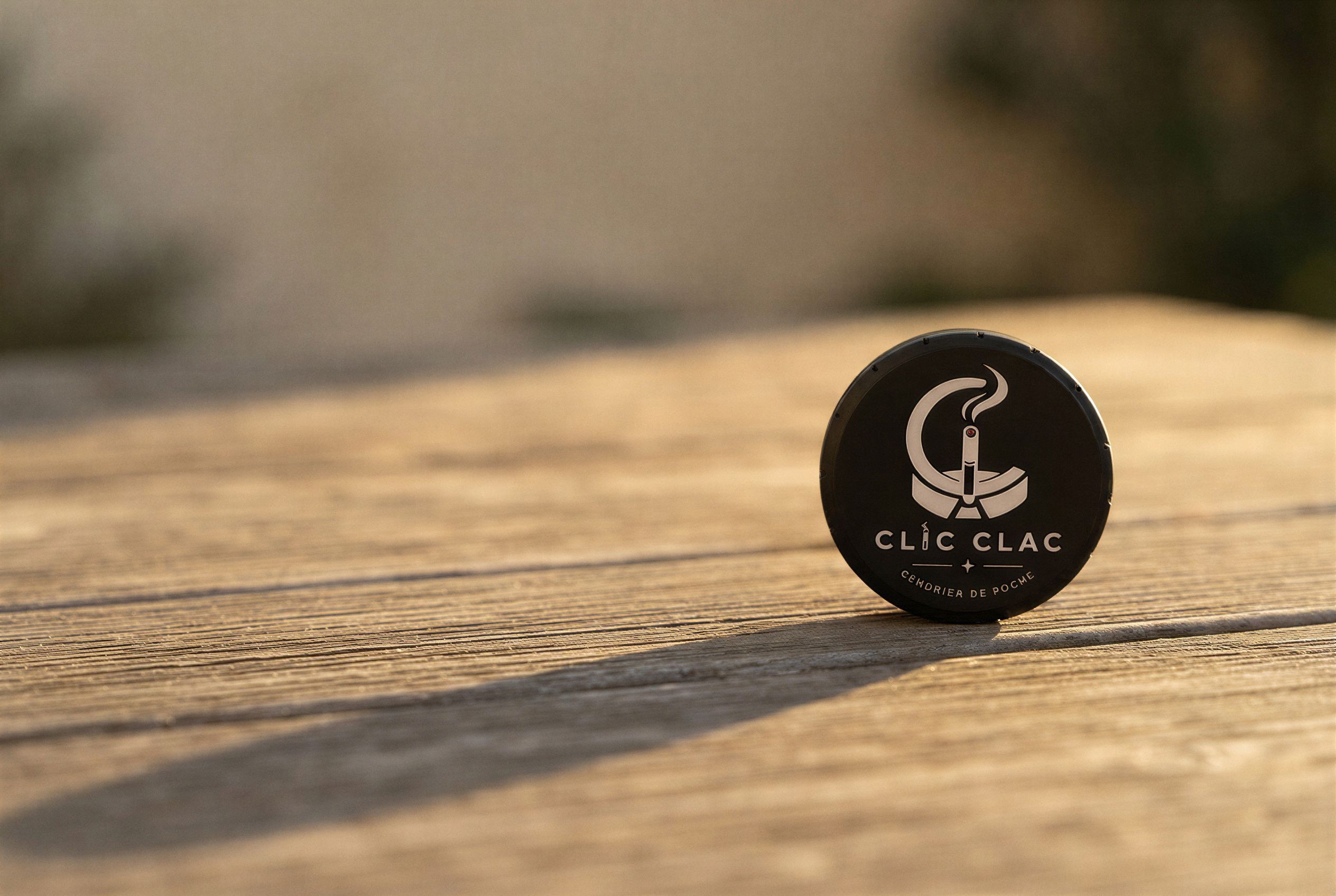 Un CLIC CLAC noir debout sur une table en bois, au soleil du soir.